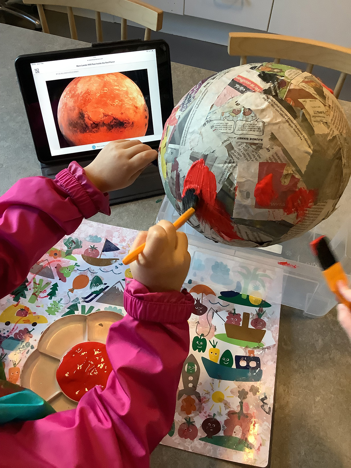 Barn målar en ballong täckt av tidningar och tapetklister till en planet